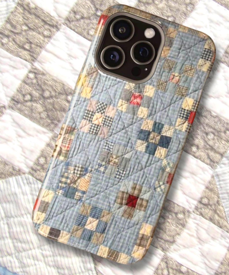 Puede incluir: Una funda para smartphone con un patr&oacute;n de tela acolchada en azul claro y una cuadr&iacute;cula de peque&ntilde;os cuadrados en tonos azul, crema y rojo. El dise&ntilde;o imita un edred&oacute;n de patchwork tradicional con l&iacute;neas de costura diagonales visibles.