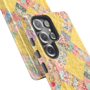 May include: A smartphone case featuring a yellow and multi-colored patchwork quilt pattern. The case has a black camera module cutout with multiple circular lens openings and black side buttons, showcasing a detailed fabric-like design.