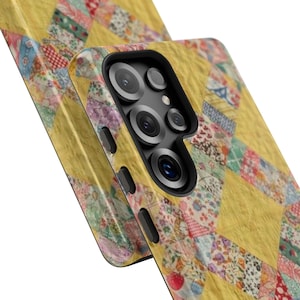 May include: A close-up of two phone cases. The cases feature a patchwork quilt design with yellow, red, blue, and green fabric squares. The phone case on the right has a camera lens and buttons.