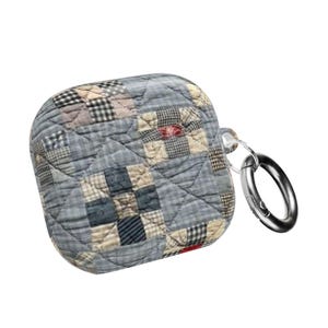 May include: A quilted AirPod case in a patchwork design. The case features a mix of blue, beige, and red squares, with a silver-colored metal ring attached for easy carrying. The case has a soft, padded appearance.