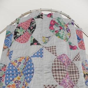 May include: A quilted shower curtain featuring a light gray background with a repeating pattern of large, multicolored circular patches. Each circle contains various floral, geometric, and polka dot prints in shades of pink, blue, green, and brown.