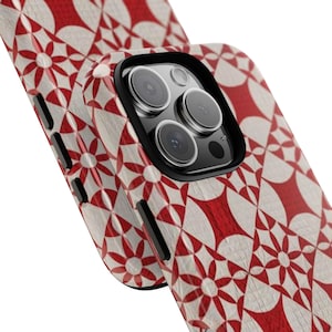 May include: A close-up of a phone case with a red and white geometric floral pattern. The case has a black border around the camera lenses. The design is repeated on the side of the phone.