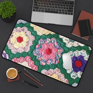 May include: A rectangular mouse pad with a colorful floral quilt pattern. The design features hexagonal shapes with red, pink, yellow, and purple floral patterns, set against a green background. A white mouse sits on the pad, with a laptop, notebooks, and a coffee cup nearby.