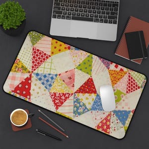 May include: A rectangular mouse pad with a patchwork quilt design. The quilt pattern features various colorful triangles with floral, polka dot, and plaid patterns. A white mouse and a laptop are on the dark surface.
