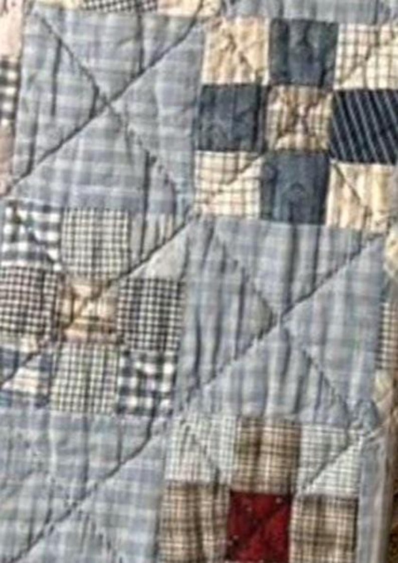 Puede incluir: Una colcha de patchwork que presenta una variedad de cuadrados de tela en azul, blanco y beige con patrones de cuadros, vichy y lisos. El textil est&aacute; cosido con un dise&ntilde;o de acolchado de rejilla diagonal, destacando un solo cuadrado rojo oscuro.