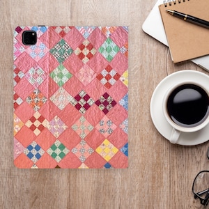 May include: A pink quilted tablet case with a patchwork design. The case features a variety of small, square fabric patches in shades of pink, red, green, and blue. The case is on a wooden surface, next to a cup of coffee and a laptop.