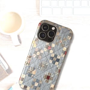 Puede incluir: Una funda para smartphone con un patr&oacute;n de tela acolchada en azul claro, blanco y beige, con una cuadr&iacute;cula de peque&ntilde;os cuadrados y l&iacute;neas de costura diagonales. La funda tiene un recorte para un sistema de c&aacute;mara de triple lente.