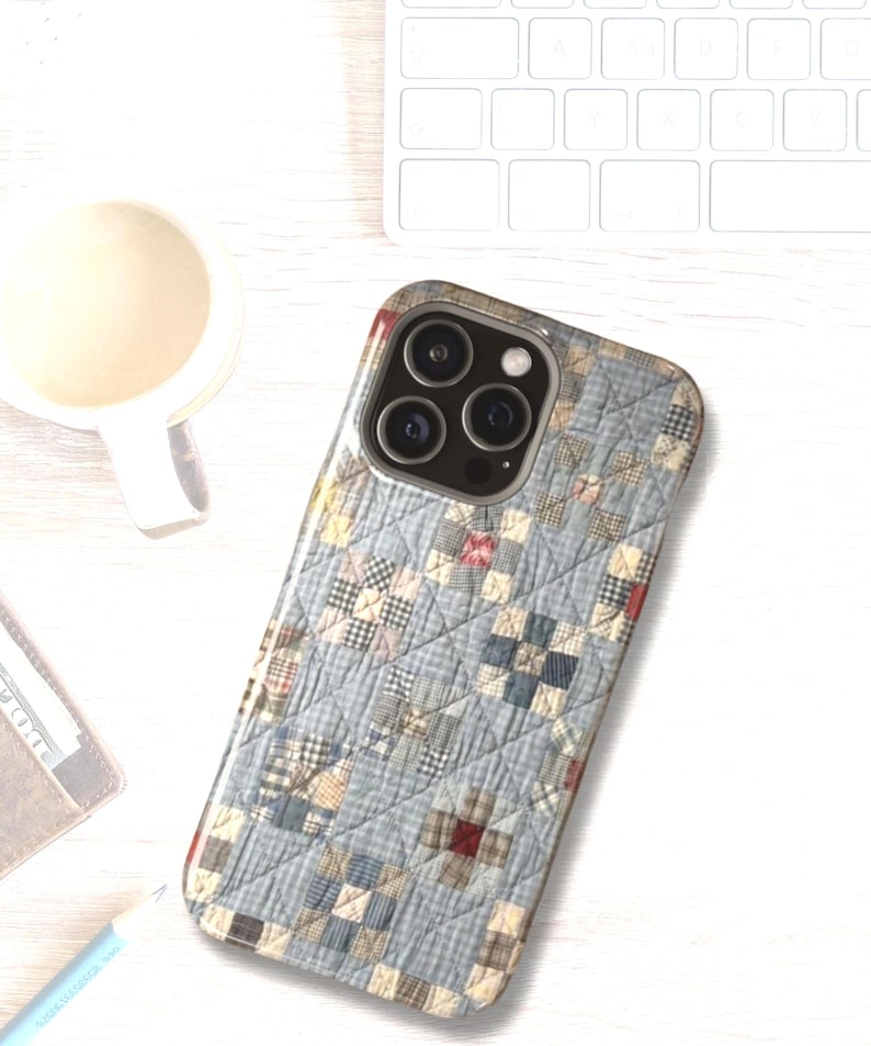 Puede incluir: Una funda para smartphone con un patr&oacute;n de tela acolchada en azul claro, blanco y beige, con una cuadr&iacute;cula de peque&ntilde;os cuadrados y l&iacute;neas de costura diagonales. La funda tiene un recorte para un sistema de c&aacute;mara de triple lente.
