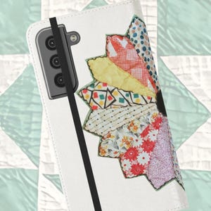May include: White phone case with a colorful, patchwork flower design. The flower petals are made of various patterned fabrics in red, yellow, and blue. A black elastic band secures the case closed.
