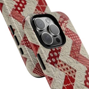 May include: A phone case with a quilted design in red and off-white. The case features a repeating pattern of red shapes and white stitching, with a black camera lens surround.