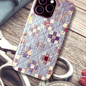 Puede incluir: Una funda para smartphone con un patr&oacute;n de tela acolchada en azul claro y blanco, con peque&ntilde;os parches cuadrados en tonos morados, rojos y amarillos. La funda tiene un recorte para triple c&aacute;mara y un aspecto texturizado y cosido.