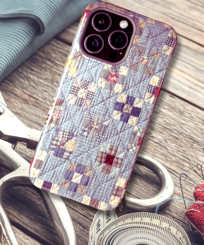Puede incluir: Una funda para smartphone con un patr&oacute;n de tela acolchada en azul claro y blanco, con peque&ntilde;os parches cuadrados en tonos morados, rojos y amarillos. La funda tiene un recorte para triple c&aacute;mara y un aspecto texturizado y cosido.