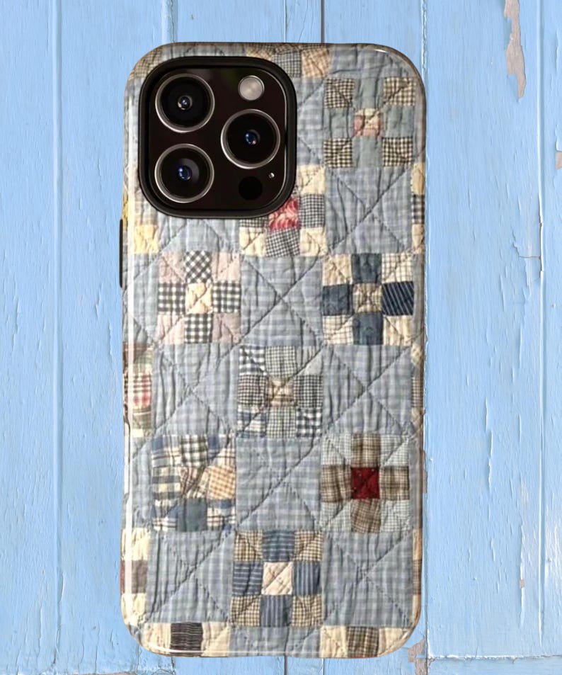 Puede incluir: Una funda para smartphone con un estampado de patchwork acolchado en tonos azul claro, crema y azul marino. El dise&ntilde;o muestra una cuadr&iacute;cula de bloques cuadrados con diversas texturas de cuadros y rayas, acentuados por peque&ntilde;os cuadrados rojos y tostados.