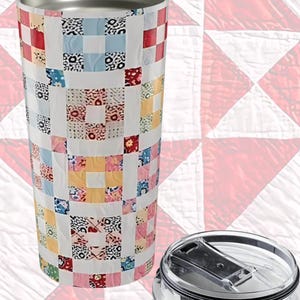 May include: A stainless steel tumbler with a white background and a patchwork quilt design in red, blue, yellow, and black. The lid is clear with a black rim. The tumbler is designed to keep drinks hot or cold.