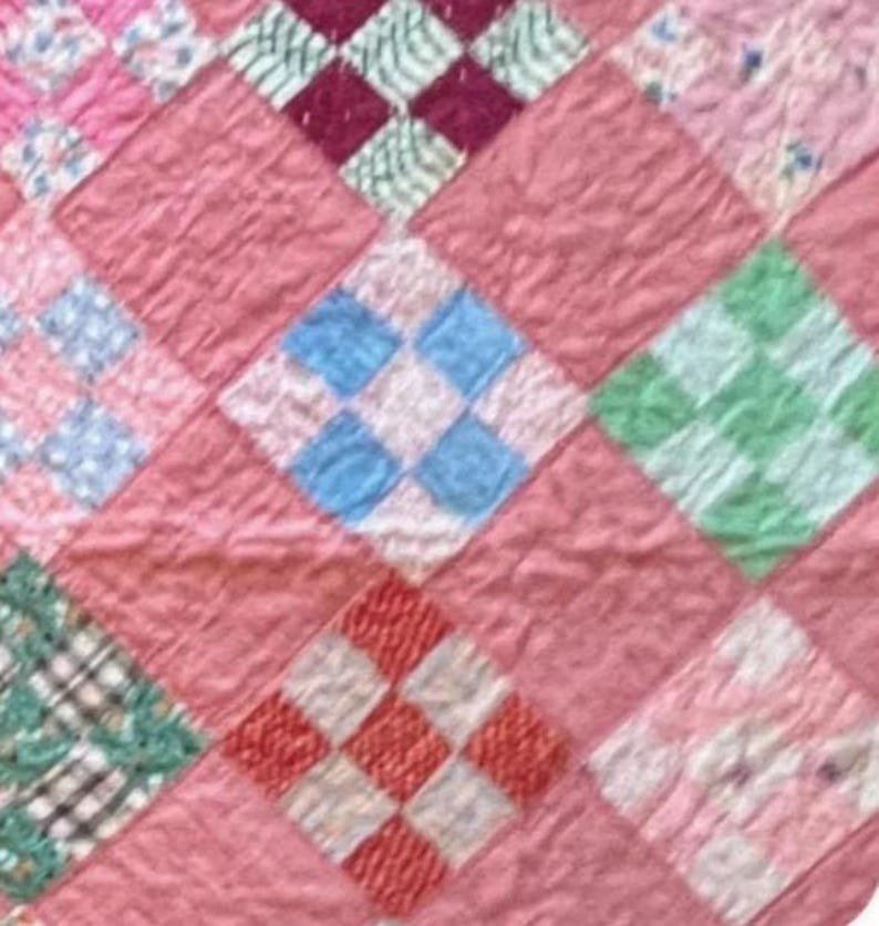 May include: Close-up of a vintage quilt with a patchwork design. The quilt features a repeating pattern of diamond shapes in various colors, including pink, blue, green, red, and white. The quilt has a soft, textured appearance, suggesting it is made of fabric.