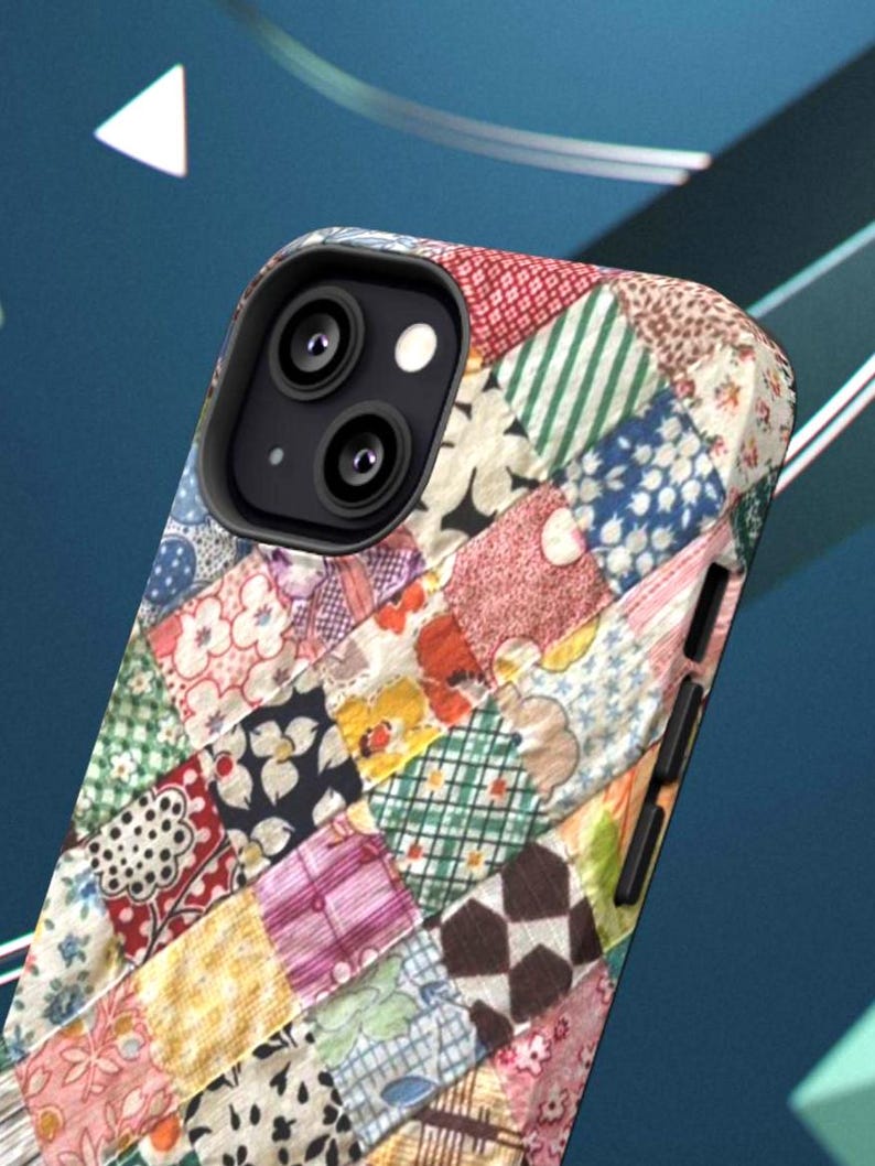 Op de afbeelding: Een smartphonehoesje met een veelkleurig patchwork-quiltpatroon met diverse bloemmotieven, geometrische vormen en ruitjes in tinten rood, blauw, groen, geel en wit, voorzien van zwarte zijknoppen en een zwarte omlijsting voor de cameralens.