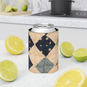 May include: A quilted can cooler featuring a patchwork design with navy blue polka dots and light blue diamonds. The cooler is holding a silver can, with cut lemons and limes in the foreground.