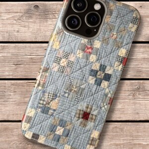 Puede incluir: Una funda para smartphone con un patr&oacute;n impreso de tela acolchada azul y blanca con una cuadr&iacute;cula de peque&ntilde;os cuadrados. El dise&ntilde;o incluye sutiles acentos rojos y tostados dentro de los bloques de patchwork, con una textura de costuras en forma de diamante.