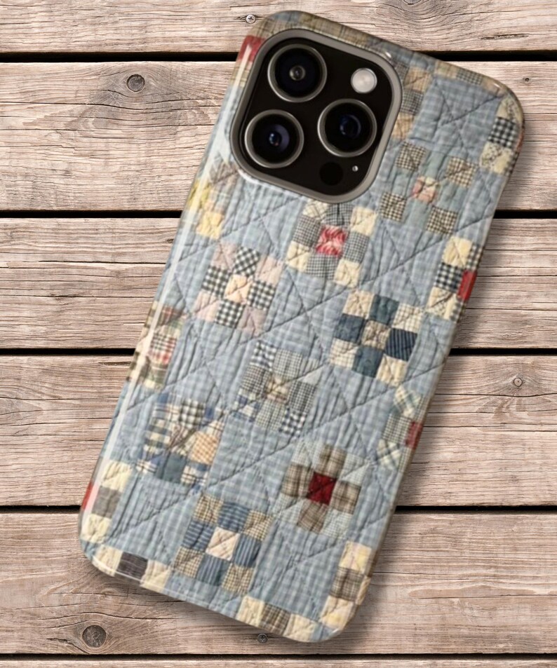 Puede incluir: Una funda para smartphone con un patr&oacute;n impreso de tela acolchada azul y blanca con una cuadr&iacute;cula de peque&ntilde;os cuadrados. El dise&ntilde;o incluye sutiles acentos rojos y tostados dentro de los bloques de patchwork, con una textura de costuras en forma de diamante.