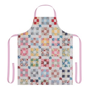 May include: A patchwork apron with a light pink neck strap and waist ties. The apron features a repeating pattern of colorful squares in shades of red, pink, blue, and yellow on a white background. The apron is designed for kitchen use.