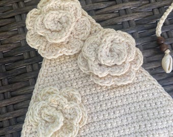 Puede incluir: Top de ganchillo color crema con tres aplicaciones de flores. El top tiene forma triangular y una correa trenzada. Una concha y cuentas de madera están unidas a la correa. El ganchillo es detallado y las flores son tridimensionales.