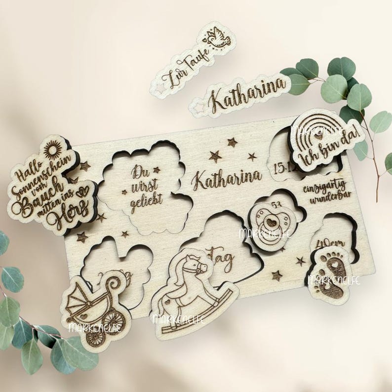 May include: Wooden puzzle with a variety of cutouts and text, including "Hallo Sonnenschein vom Bauch mitten ins Herz", "Du * wirst geliebt", "Katharina", "Zur Taufe", "Katharina 15.1", "Ich bin da!", "Tag", "53 cm", "einzigartig wunderbar", "40 cm", and a baby footprint.