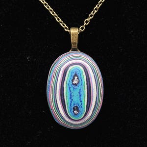 May include: A pendant necklace with an oval-shaped, multi-colored agate stone. The stone has a swirling pattern of white, pink, blue, and black.