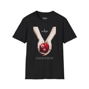 May include: Black t-shirt featuring the Twilight movie poster. The graphic shows a red apple with a bite taken out of it, held by two hands. The text "twilight" is above the apple, and "THE #1 NEW YORK TIMES BESTSELLER BY STEPHENIE MEYER" is below.