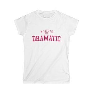 Puede incluir: Camiseta blanca con el texto rosa "A Little Bit Dramatic". Esta prenda de cuello redondo y mangas cortas es una opción sencilla y versátil para un look casual.