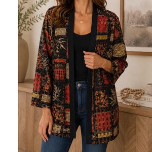 Könnte beinhalten: Kimono-Jacke im Patchwork-Design mit roten, goldenen und schwarzen Quadraten und floralen Mustern. Die Jacke hat einen schwarzen Besatz und wird offen getragen. Die Ärmel sind dreiviertellang.
