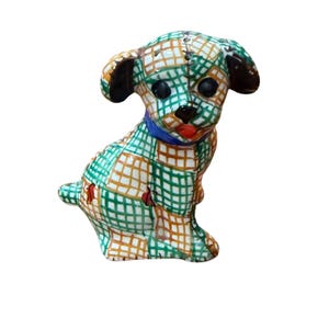 Könnte beinhalten: Eine Keramik-Hundefigur mit einem Patchwork-Muster aus grünen und orangefarbenen Gitterlinien. Der Welpe hat große schwarze Augen, eine kleine schwarze Nase, eine rote Zunge und ein einfarbig blaues Halsband. Die Ohren sind dunkelbraun.