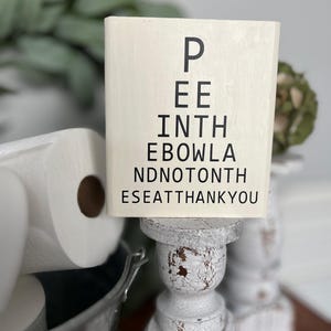May include: White wooden sign with black text that reads "P EE INTH EBOWLA NDNO TONTH ESEAT THANKYOU". The sign is on a white pedestal.
