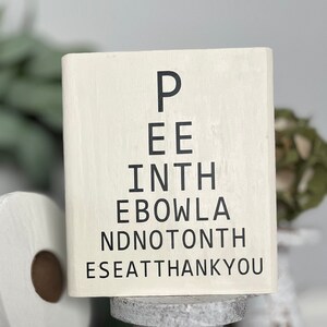 May include: White wooden sign with black text that reads "Pee in the bowl and not on the seat thank you".