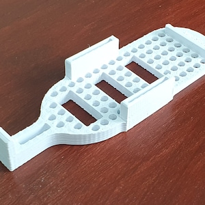 Puede incluir: Soporte para teléfono blanco de plástico impreso en 3D con un patrón de cuadrícula y tres ranuras para sujetar teléfonos.