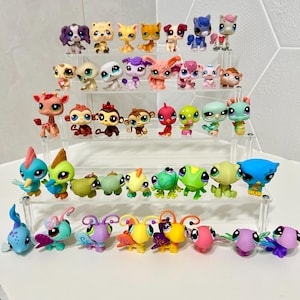 Peut inclure: Une collection de trente-cinq figurines d'animaux en plastique disposées sur un présentoir en acrylique transparent à quatre niveaux. Les figurines représentent divers animaux comme des chats, chiens, singes, oiseaux, grenouilles et insectes.