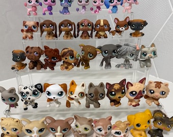 May include: A collection of thirty-three small plastic dog figurines with large eyes, arranged on a four-tiered clear acrylic display stand. The figures feature various breeds, colors, and patterns, including poodles, spaniels, and terriers.