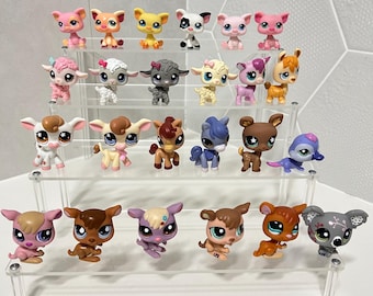 May include: A collection of twenty-four small, stylized animal figurines arranged on a four-tiered clear acrylic display stand. The figures feature large eyes and various colors, including pink, brown, white, gray, and yellow, representing diverse creatures like lambs, dogs, and other animals.