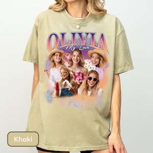 May include: A khaki-coloured t-shirt featuring a graphic print with the text "OLIVIA My Love" in a gradient font. The design includes a collage of four images of a woman wearing hats and sunglasses, surrounded by a soft purple and orange glow.