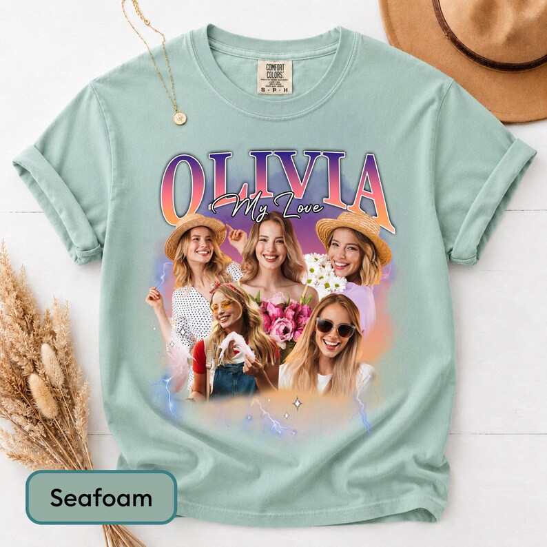 May include: A seafoam green short-sleeve t-shirt featuring a graphic print of four individuals with the text OLIVIA My Love in a gradient font. The design includes a purple and orange sunset background with lightning accents and a Comfort Colors label.