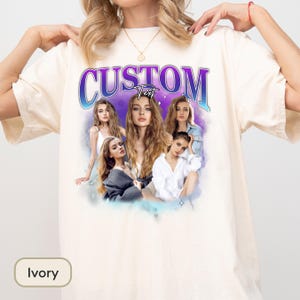 May include: An ivory short-sleeve t-shirt featuring a graphic print with the word CUSTOM in large purple and blue gradient letters. Below the text, a collage of five photographs of the same person with long wavy hair is set against a purple cloud.