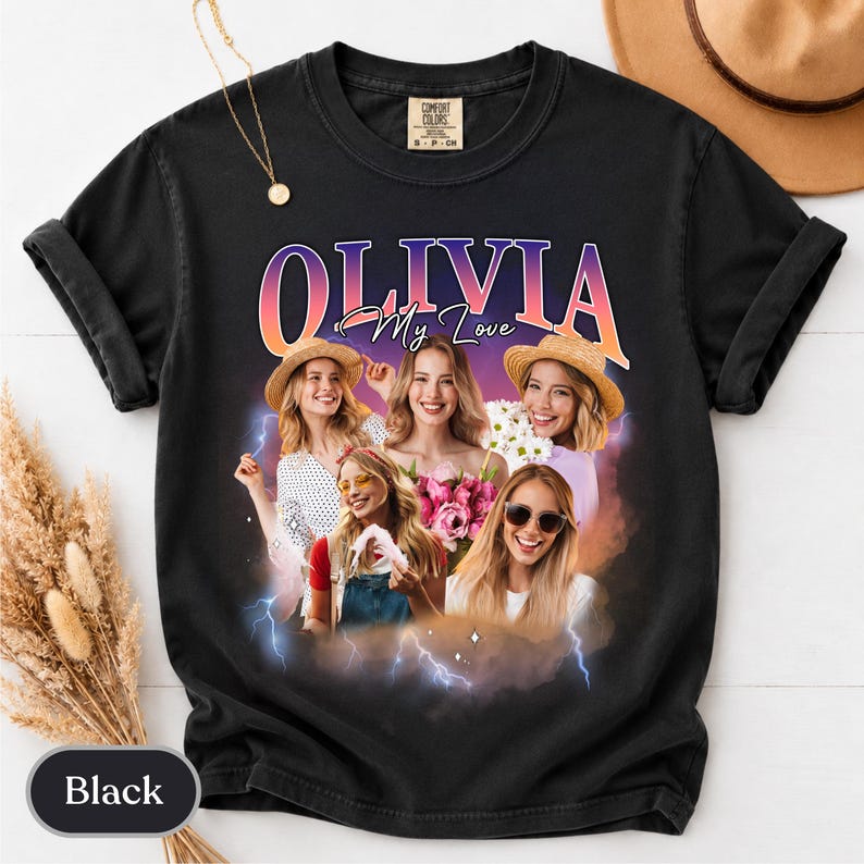 May include: A black short-sleeve t-shirt featuring a graphic print with the text "OLIVIA My Love" in a gradient font. The design includes a collage of four smiling individuals, pink flowers, and blue lightning bolts against a purple sunset background.