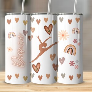May include: Three white stainless steel tumblers with a dancer silhouette, rainbows, hearts, and flowers in shades of brown, pink, and gold. The tumbler on the left has the word "Dance" in neon pink lettering.