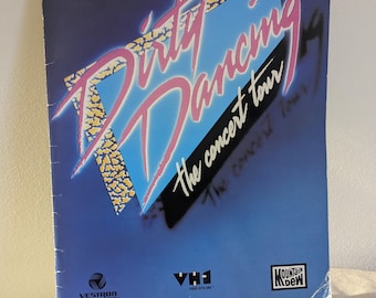 May include: A vintage "Dirty Dancing: The Concert Tour" program. The cover features the title in pink and yellow, set against a blue and black background. Includes the logos for Vestron Pictures, VH1, and Mountain Dew.