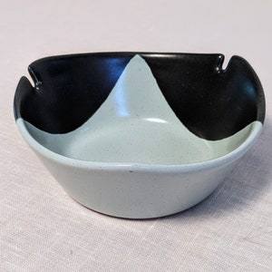 May include: A light blue and black ceramic ashtray with a geometric design. The ashtray has a rounded shape and a wide, shallow bowl.