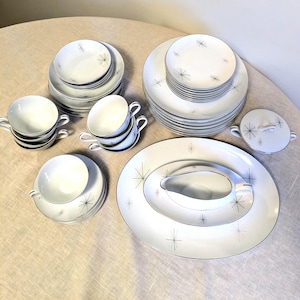 Könnte beinhalten: Ein Set weißes Geschirr mit einem schwarzen Sternmuster. Das Set enthält Teller, Schalen, Tassen, Untertassen, eine Sauciere und eine Servierplatte.