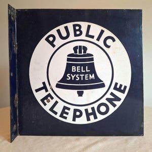 Teléfono público de metal esmaltado antiguo de los años 1940-1950 con sistema de timbre, letrero azul y blanco de doble cara que ha estado en interiores la mayor parte de su vida. 18" x 18"