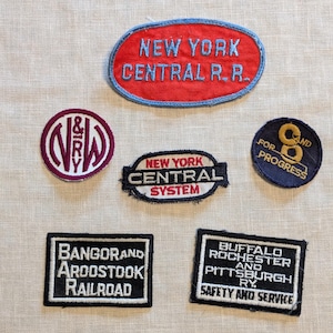 May include: A collection of vintage railroad patches. The patches are embroidered with the names of different railroads, including "New York Central R.R.", "Bangor and Aroostook Railroad", "Buffalo Rochester and Pittsburgh Ry", "N&W Ry", "New York Central System", and "C&O for Progress".