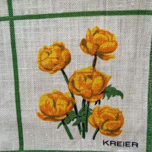 May include: A white linen handkerchief with a green border and grid pattern. The handkerchief features a cluster of orange and yellow flowers with green stems and leaves. The word "KREIER" is printed in black.