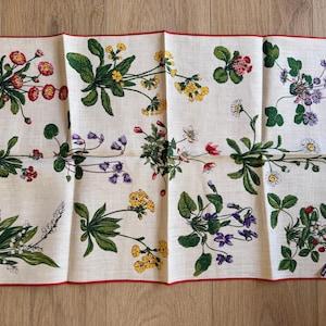 May include: A white linen handkerchief with a red border, adorned with floral illustrations in red, yellow, purple, and white. The design features various flowers and green leaves, creating a botanical theme.