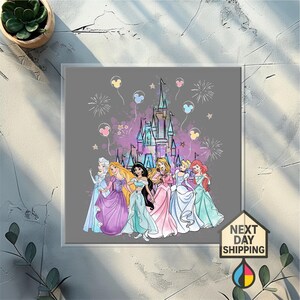 May include: A framed print featuring Disney princesses in front of a castle with fireworks and balloons. The princesses are wearing colorful gowns. The background is gray with purple and pink accents. The print includes the text "NEXT DAY SHIPPING".
